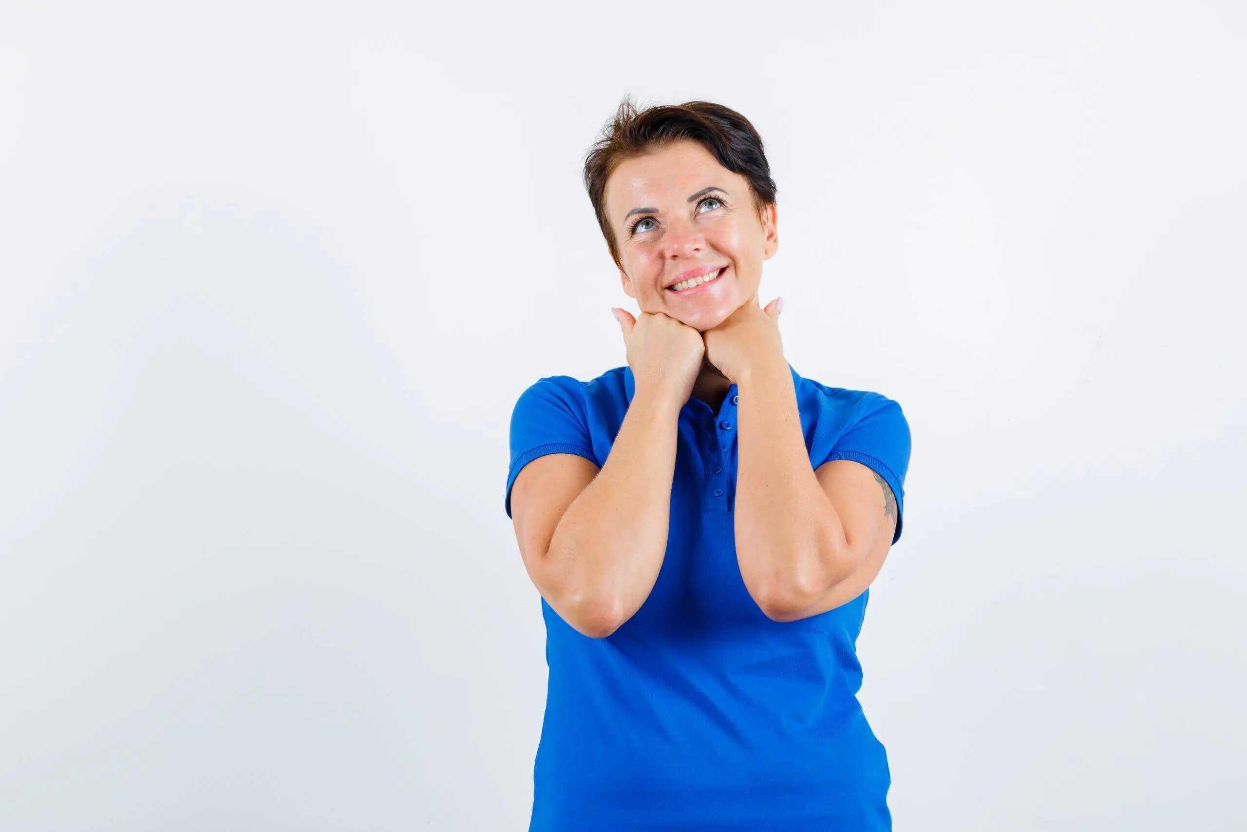 mature woman propping chin on hands in blue t-shirt and looking dreamy. front view.