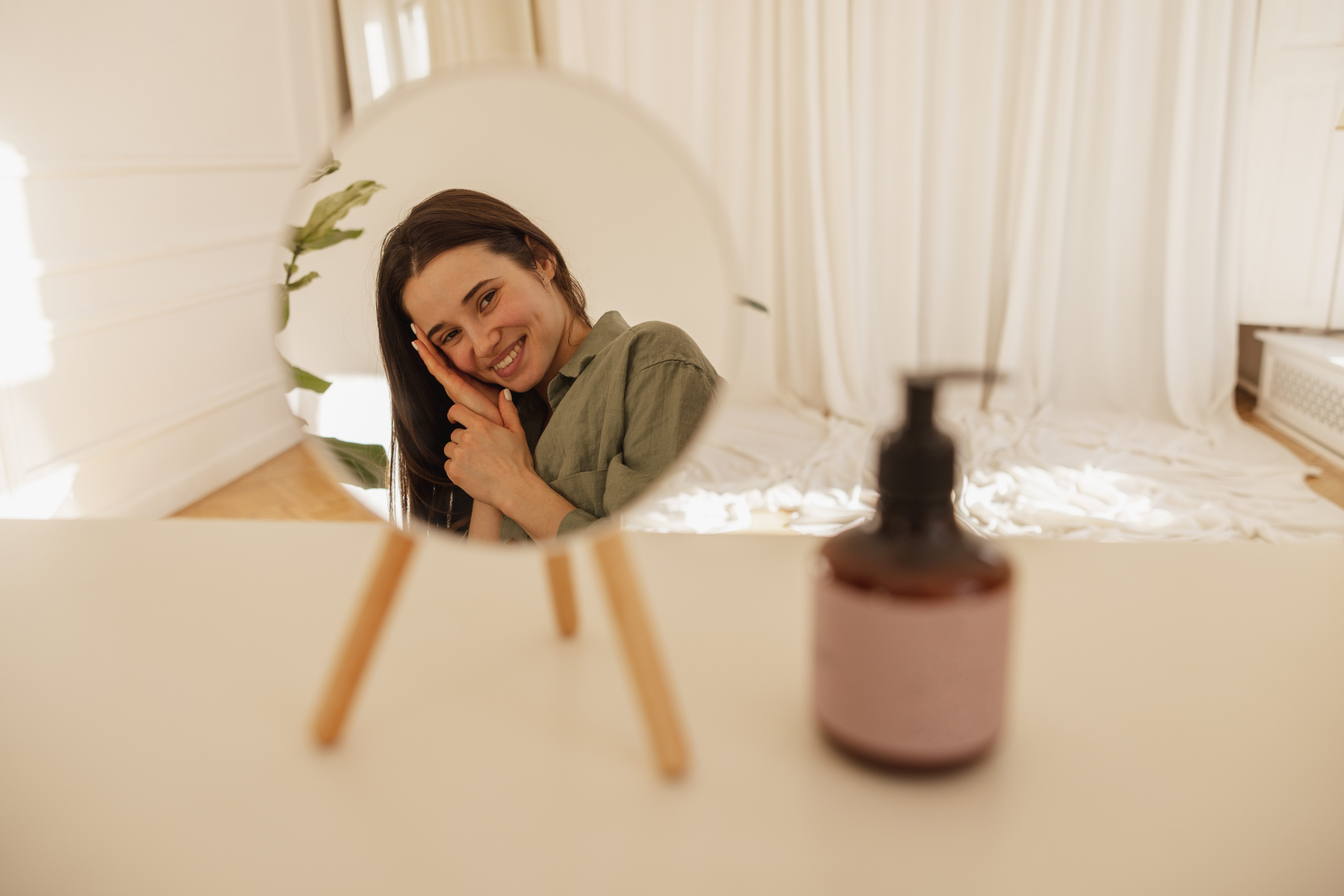 beautiful-young-caucasian-girl-admires-her-appearance-while-looking-camera-through-mirror-brunette-green-shirt-is-ready-apply-makeup-skin-care-hydration-concept