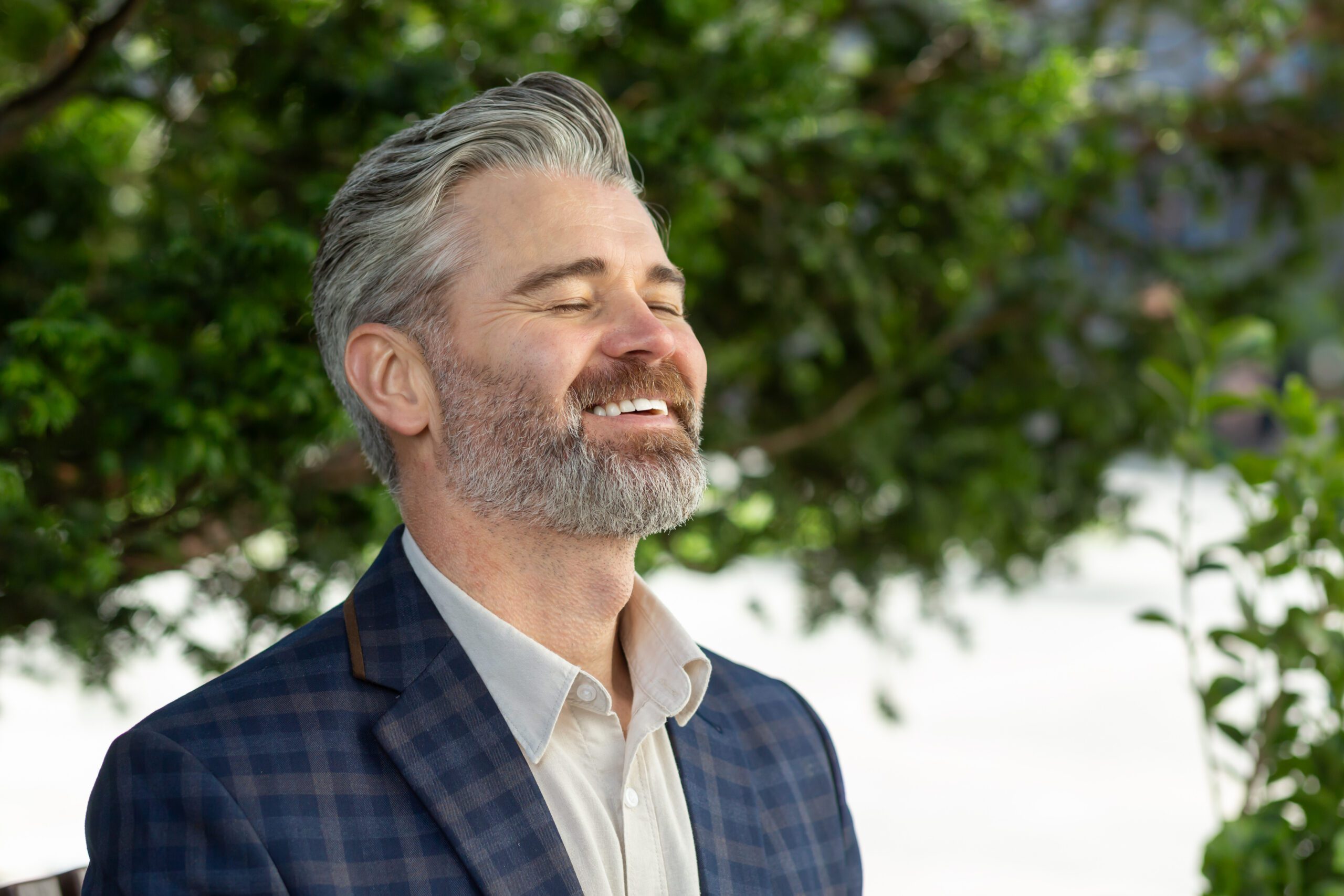 Portrait of a happy senior businessman in a suit, enjoying success outside an office environment with trees in the background.
