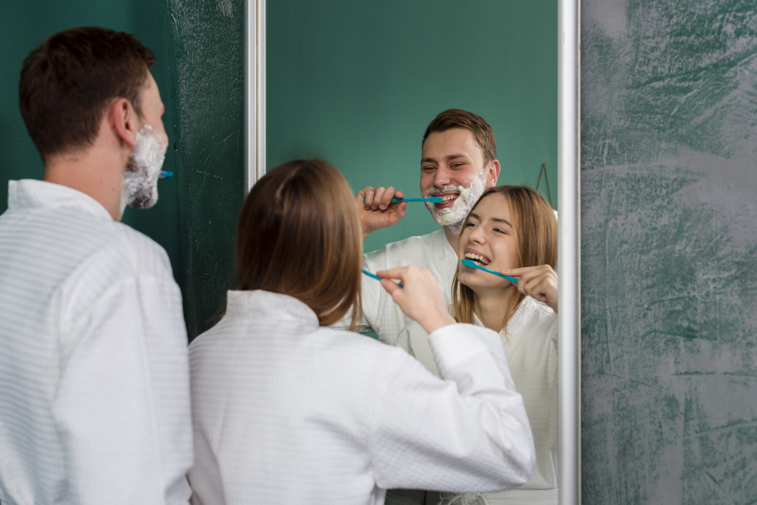 couple-wearing-bathrobes-brushing-teeth-mirror