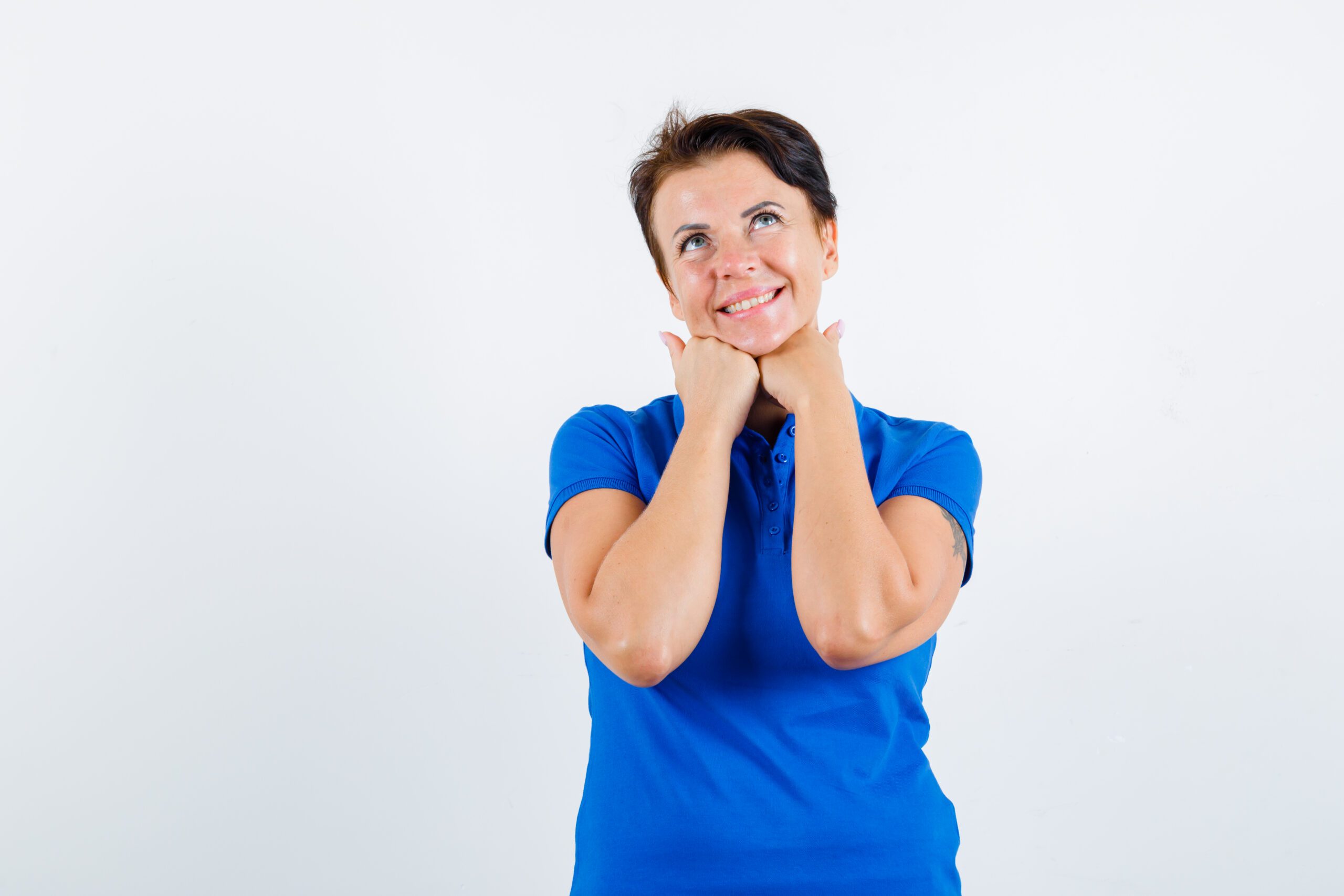 mature woman propping chin on hands in blue t-shirt and looking dreamy. front view.