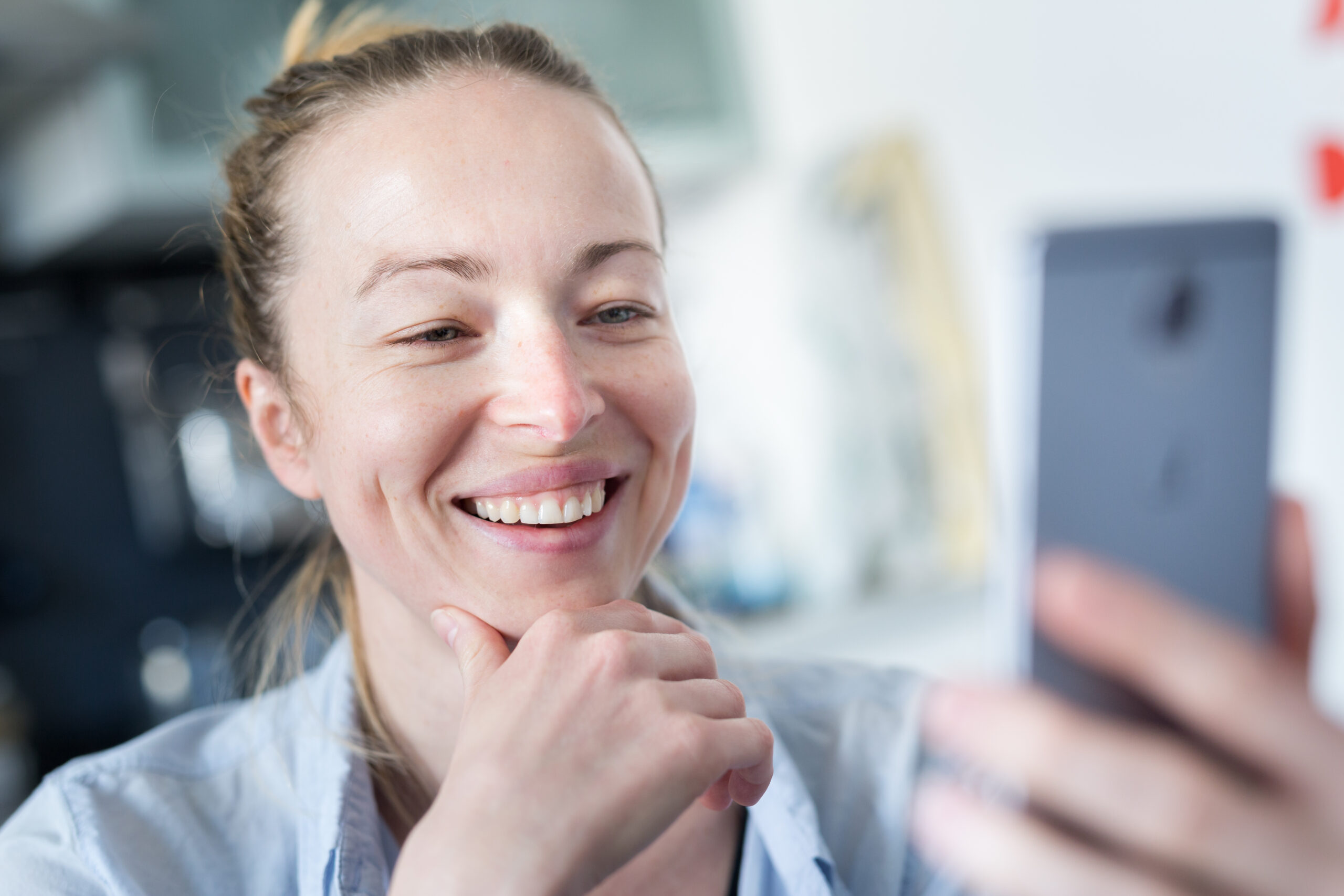 Young smiling cheerful woman indoors at home kitchen using social media apps on phone for video chatting and stying connected with her loved ones. Stay at home, social distancing lifestyle.