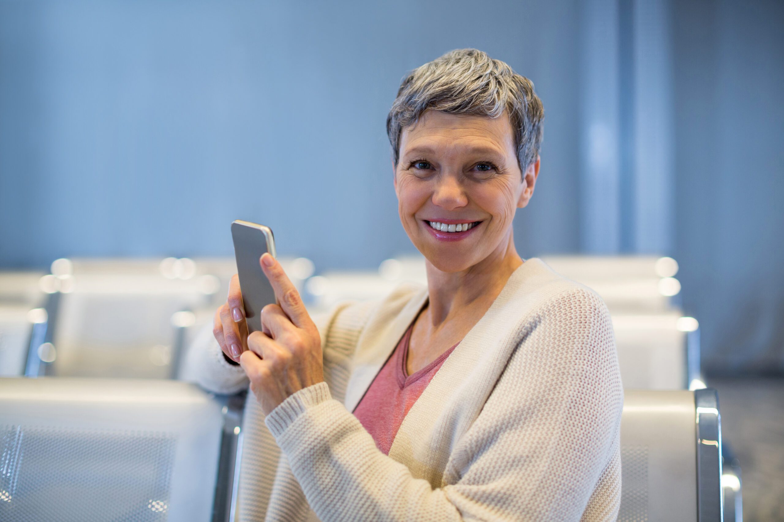 Portrait of smiling woman sitting with mobile phone in waiting area at airport terminal